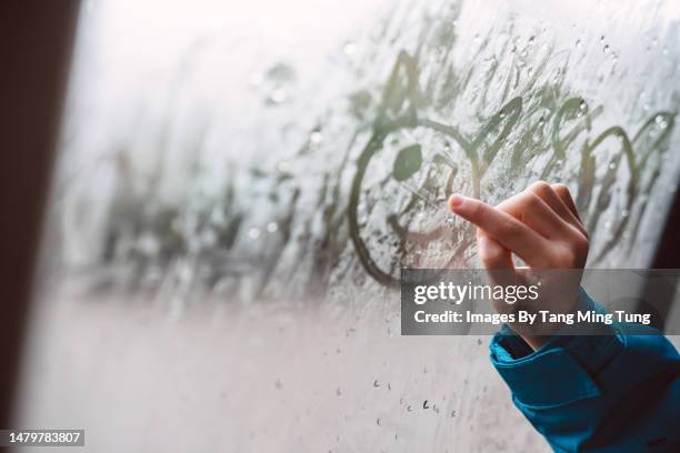 close-up of a girl’s hand drawing on condensed car window with finger while travelling in car - condensación fotografías e imágenes de stock