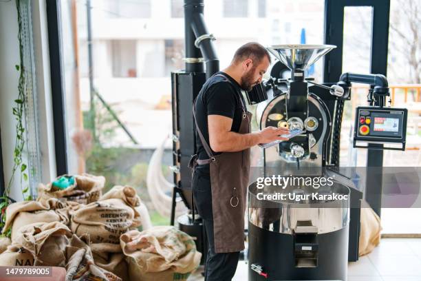 man using digital tablet in front of coffee roasting machine - coffee roasting stock pictures, royalty-free photos & images