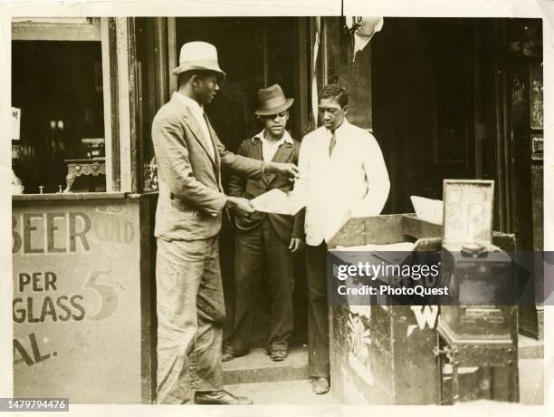 View of a customer as he buys a newspaper from a vendor on a Harlem street, New York, New York, circa 1925.