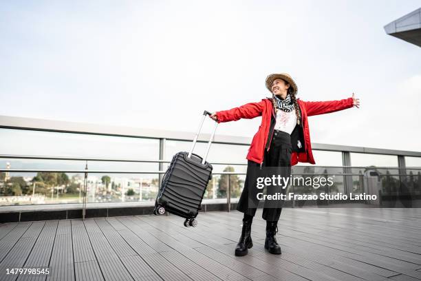 mid adult woman holding a suitcase in airport outdoors - woman flying scarf stock pictures, royalty-free photos & images
