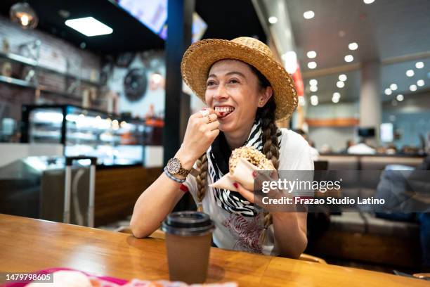 mittelerwachsene frau, die donut in einem restaurant isst - lounge restaurant stock-fotos und bilder