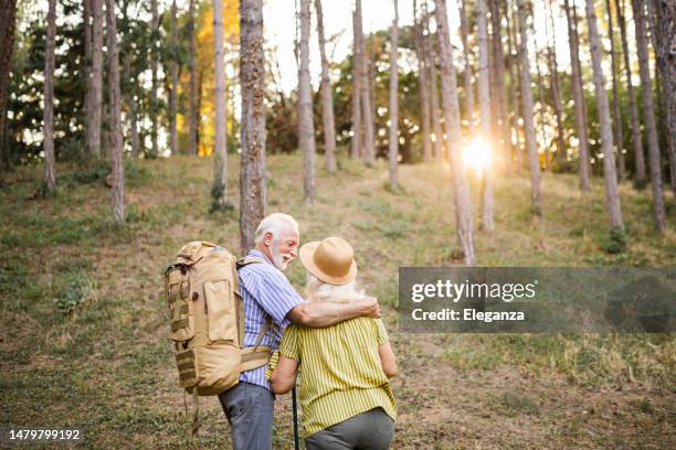 back of an elderly couple during their hike with backpacks - senior couple smiling stock pictures, royalty-free photos & images