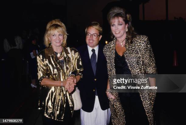 American actress Angie Dickinson, wearing a gold jacket, American film producer Allan Carr, who wears a dark blue blazer with white trousers, and...