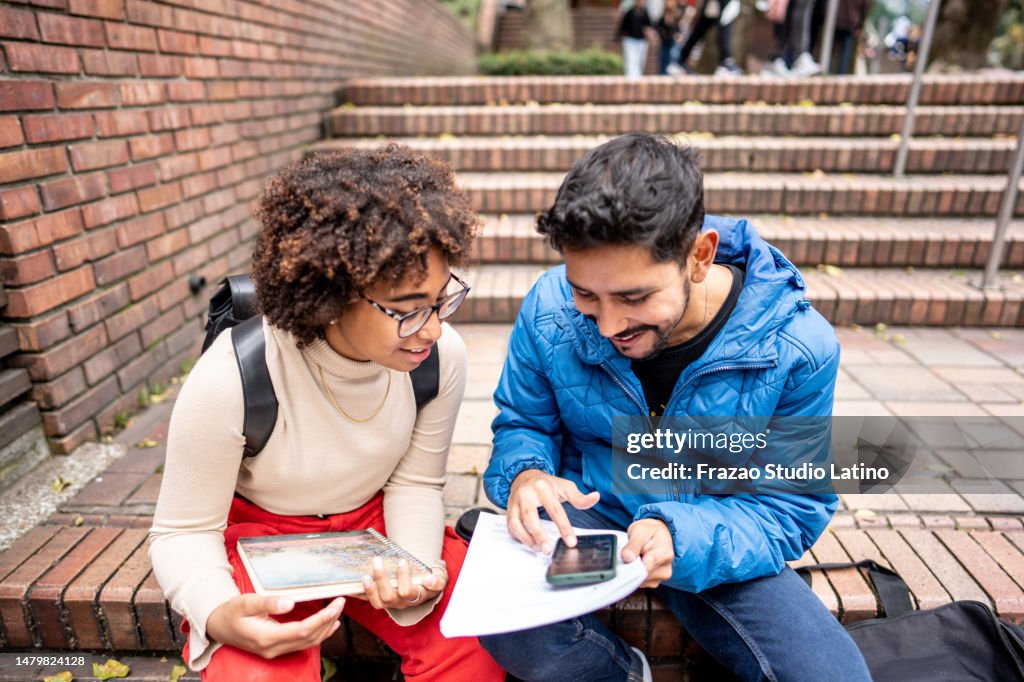 Young university students using mobile phone while study on stair outdoors