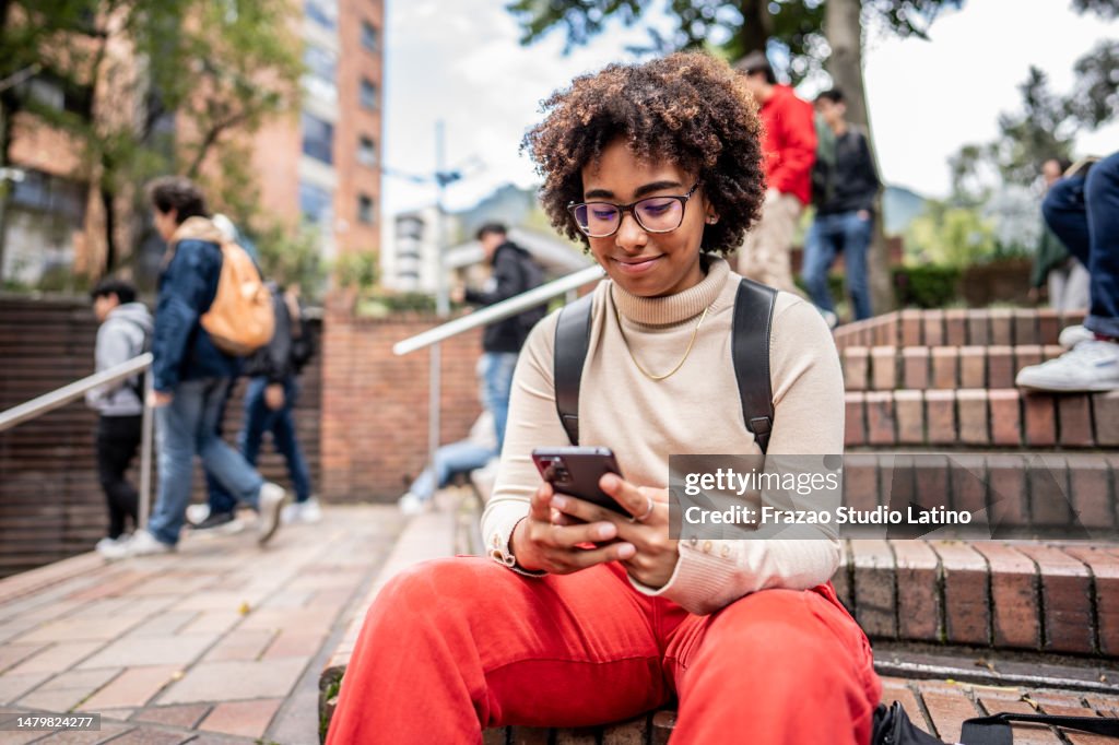 Young university student using mobile phone on stairs outdoors