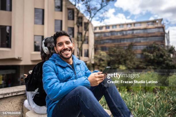 portrait of a young man using mobile phone leaning against his friend outdoors - back to back leaning stock pictures, royalty-free photos & images