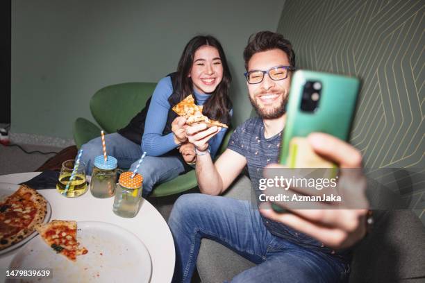 ein glücklicher, attraktiver junger erwachsener kaukasischer mann, der ein selfie mit seiner freundin an der bar macht, während er ihre pizza genießt - fotografische themen stock-fotos und bilder