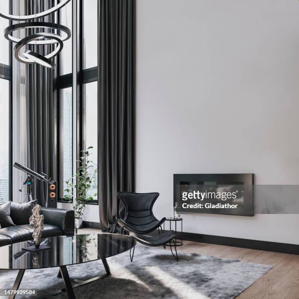 modern industrial living room with high ceilings, industrial windows, a black leather sofa, a chair, a table, and decoration in front of a high plaster wall with a fireplace - wooden floor white background stock pictures, royalty-free photos & images