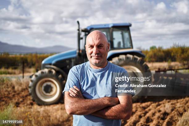 farmer looking at camera with tractor in field - agricultor imagens e fotografias de stock