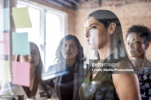 businesswomen brainstorming and looking at notes on a glass wall in conference room - senior vice president fotografías e imágenes de stock