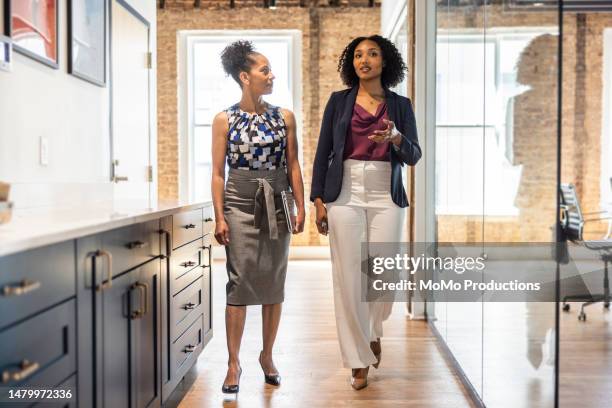 female colleagues walking down glass hallway in modern office - witte blazer stockfoto's en -beelden