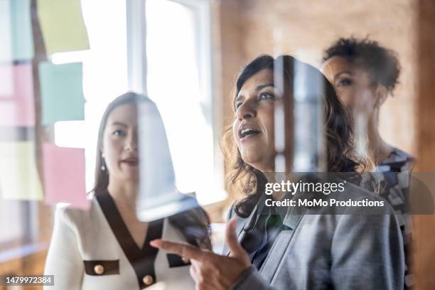 businesswomen brainstorming and looking at notes on a glass wall in conference room - barriere stock-fotos und bilder