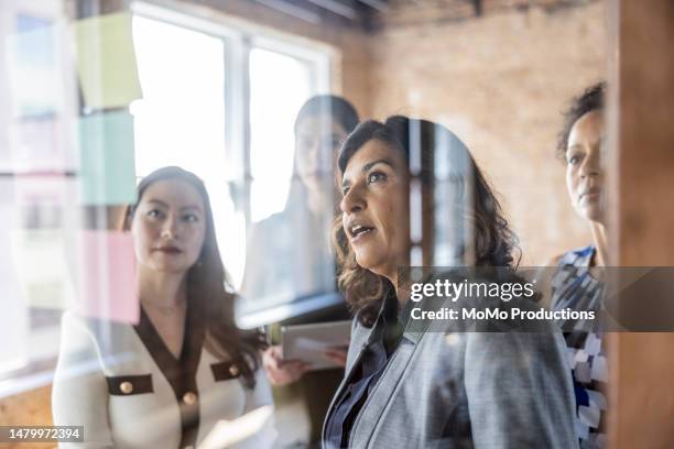 businesswomen brainstorming and looking at notes on a glass wall in conference room - barriere stock-fotos und bilder