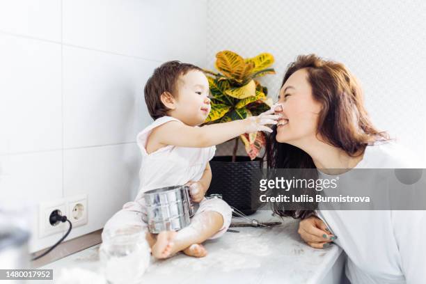 a joyful cooking experience. laughing brunette woman and baby have fun while baking, complete with a floury stroke on mom nose. - baby spielt mit essen stock-fotos und bilder
