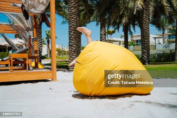 funny picture of boy bare legs are shown from yellow bean bag on the beach at tropical resort - den kopf in den sand stecken stock-fotos und bilder