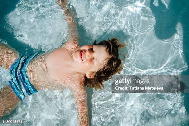 soaking up the sun: young boy swimming on the back, spent his outdoor swimming pool time on his tropical vacation. - dubai stock pictures, royalty-free photos & images