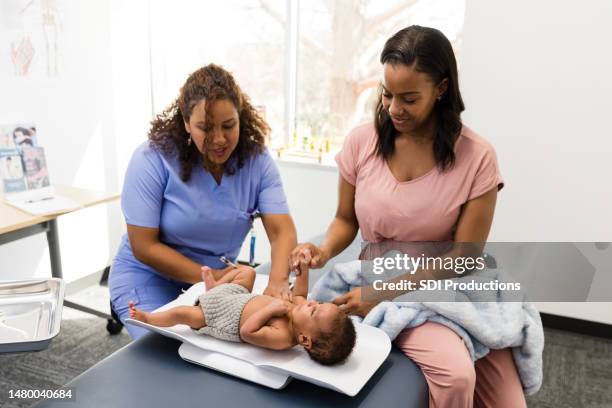 young adult mother sits close by while her son gets his weight checked at the medical office - pediatric nurse stock pictures, royalty-free photos & images