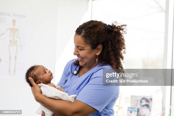 female pediatrician smiles in adoration while she holds her newest patient - nurse with baby stock pictures, royalty-free photos & images