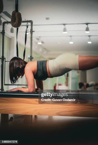 pilates workout on trapeze table, pilates instructor stretching her leg, beautiful young female pilates instructor, instructor guiding movement on pilates machine, young woman doing sports exercise - hamstring machine stock pictures, royalty-free photos & images