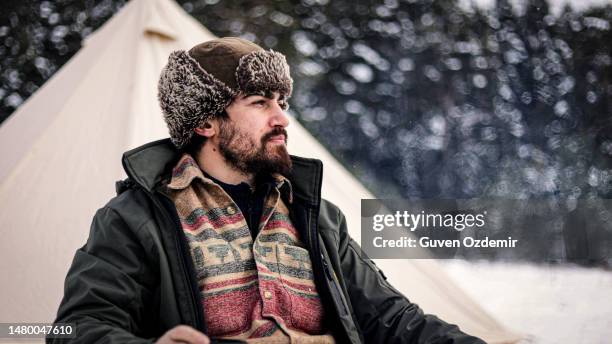 a winter camper wearing a ushanka or hunting hat, winter mountain camper drinking hot coffee by the tent, cold camper drinking hot drink, human in nature away from everything, living free in nature - hunters cap stock pictures, royalty-free photos & images