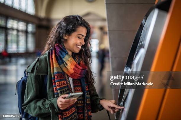 a beautiful young woman uses an atm at a metro station in barcelona, withdraws her money to go shopping - atm 個照片及圖片檔