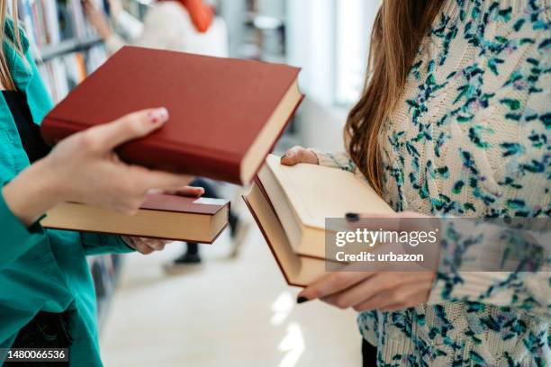 two female students exchanging books in a school library - literature student stock pictures, royalty-free photos & images