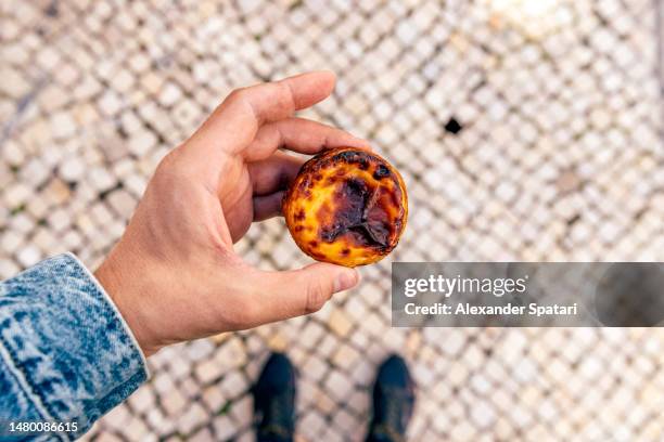 man holding pastel de nata (portuguese pastry), high angle view - pastel de nata portugal fotografías e imágenes de stock