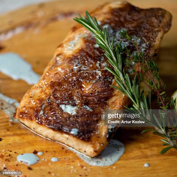 piece of fried fish with sauce and sprig of rosemary and thyme on wooden board. white fish fillet with cream sauce and herbs. close-up. top view - lampuga foto e immagini stock