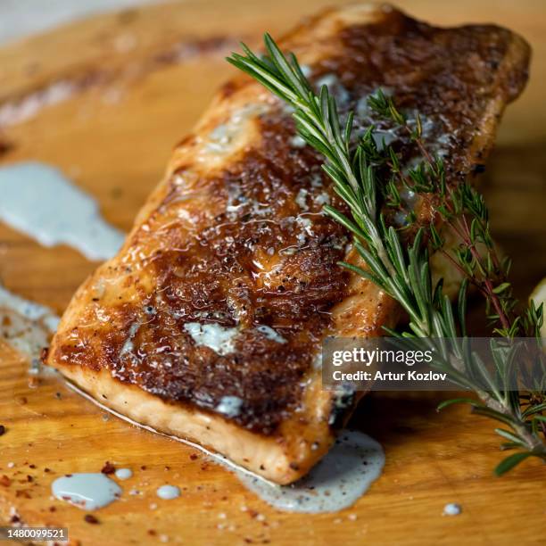 piece of fried fish with sauce and sprig of rosemary and thyme on wooden board. white fish fillet with cream sauce and herbs. close-up. top view - dolphin fish imagens e fotografias de stock