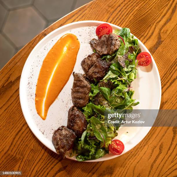 grilled pieces of meat with spinach garnish, sauce and cherry tomatoes on white plate on wooden table. grilled pork. view from above. wooden background - tenderloin filetsteak stock-fotos und bilder