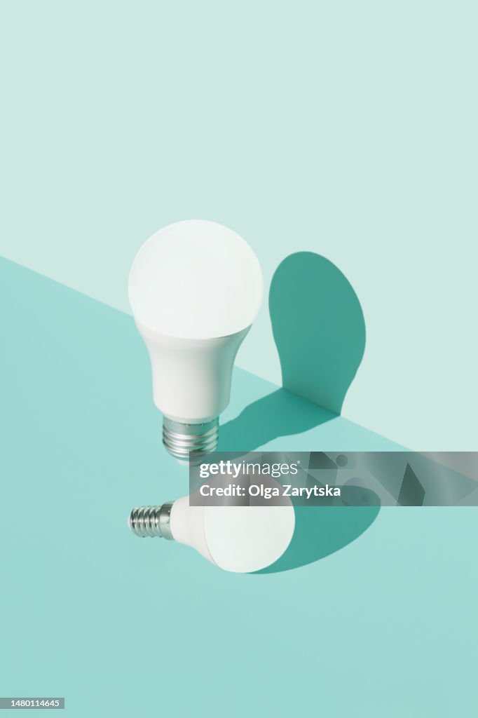 Two illuminated LED light bulbs in brightly lit on light blue background.