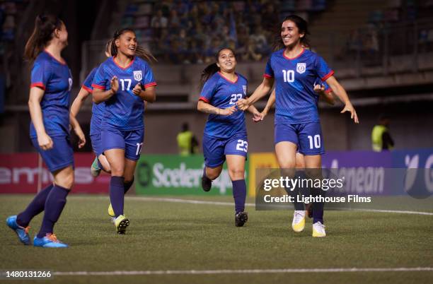 an attacking midfielder strikes a joyous smile while her teammates celebrate her accomplishment. - skilled stadium stock-fotos und bilder