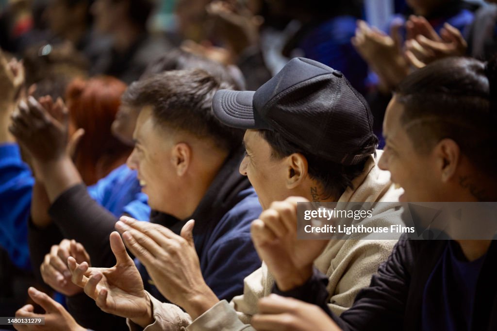 A group of three men in a crowd cheer on a sports team