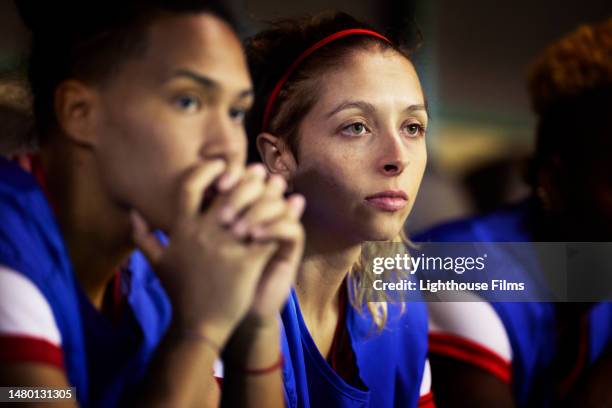female soccer players intently watch as their teammates play in a close soccer match - sad football player stock pictures, royalty-free photos & images
