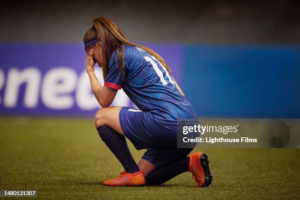 somber female soccer player kneels and holds her head in her hands in disappointment - sad football player stock pictures, royalty-free photos & images