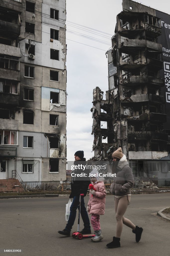 Ukrainian family walking past damaged apartment building in Borodyanka