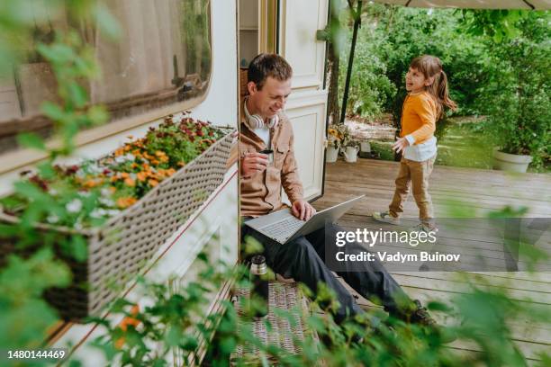 young man next to his little daughter working on a laptop while sitting on the threshold of a camper - トレーラハウス ストックフォトと画像