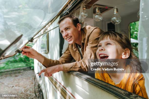 father and daughter smiling and looking out of the camper window - caravan holiday family imagens e fotografias de stock