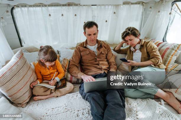 father, mother and little daughter with gadgets sitting in the camper - camping indoors stock pictures, royalty-free photos & images