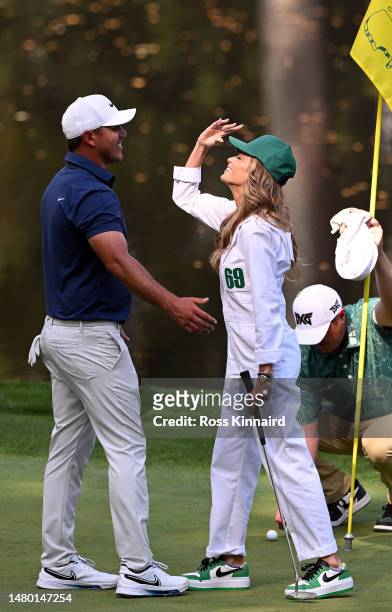 Brooks Koepka of the United States celebrates with his wife, Jena Sims Koepka, on the ninth green during the Par 3 contest prior to the 2023 Masters...