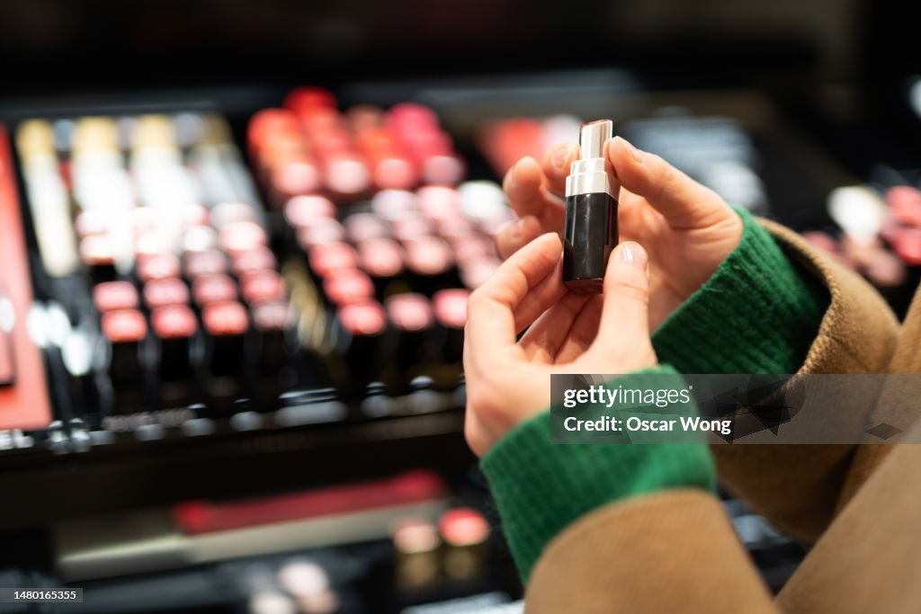 Close-up of young woman choosing lipstick at cosmetic counter in the shop