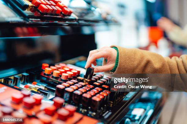 close-up of young woman choosing lipstick at cosmetic counter in the shop - perfumería fotografías e imágenes de stock