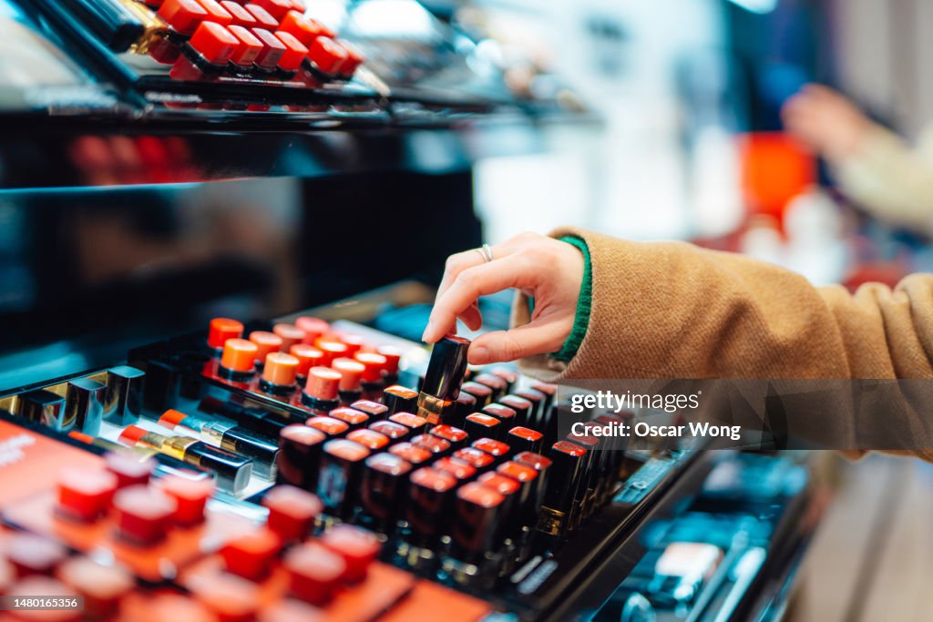 Close-up of young woman choosing lipstick at cosmetic counter in the shop