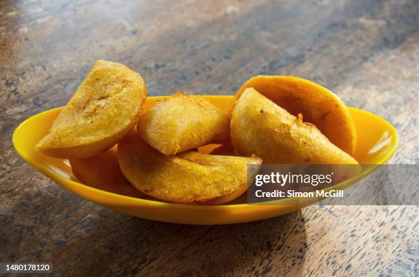 empanadas vallunas (fried corn flour pastry empanada sstuffed with potato and shredded meat) in a yellow plastic bowl on a wooden table top - cali colombia stock pictures, royalty-free photos & images