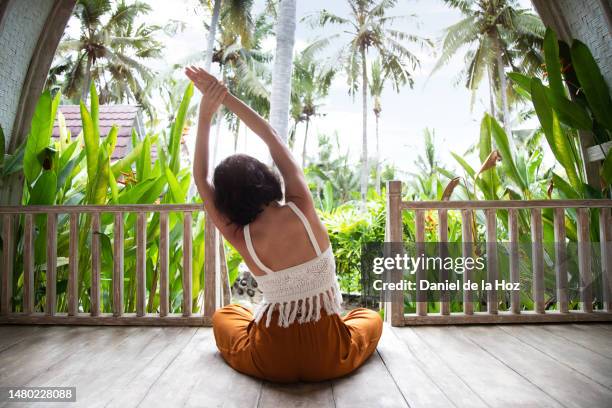 rear view of young woman doing yoga, bending side body sitting on the floor at tropical vacation resort. - bali stock pictures, royalty-free photos & images