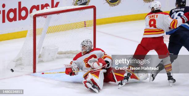 Jacob Markstrom of the Calgary Flames watches a rebound come back off the end boards as teammate Chris Tanev and Blake Wheeler of the Winnipeg Jets...