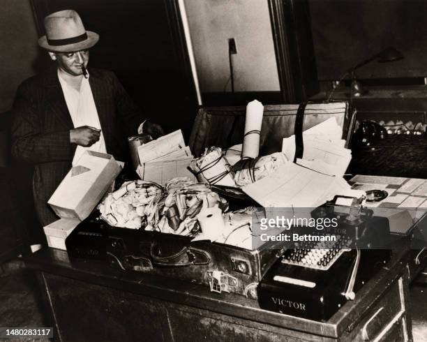 Photographer Arthur Fellig , alias 'Weegee', looks over evidence gathered in a raid on an apartment in Harlem, New York, on August 26th, 1938. In the...
