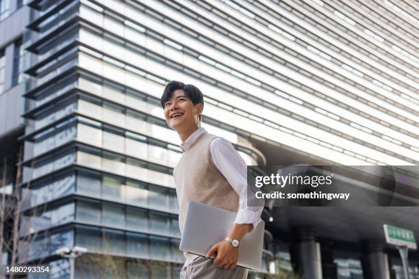 young white-collar workers walking with laptops in their arms - content japanese ethnicity stock pictures, royalty-free photos & images