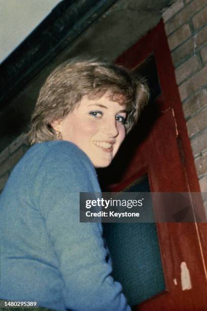 Lady Diana Spencer wearing a blue sweater and blue eye make-up turns to smile as she approaches a door, possibly London, England, September 1980.