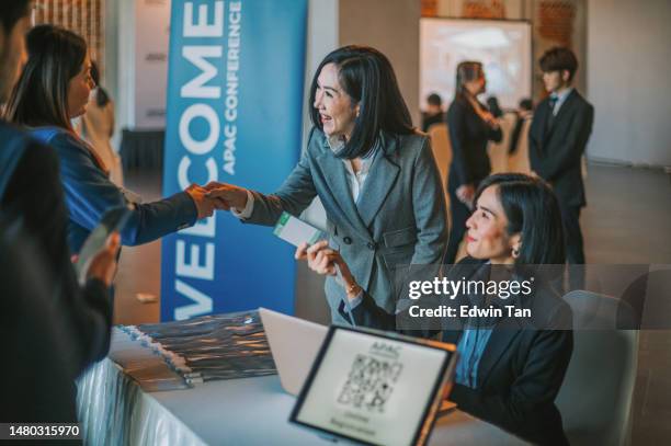 asiatische geschäftsfrau begrüßt alle gäste, die sich an der rezeption anmelden, um an einem business-konferenz-seminar teilzunehmen - einschreibungsveranstaltung stock-fotos und bilder